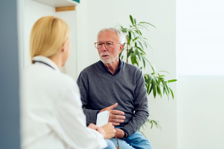 Elderly man speaks with a female doctor during a thoughtful medical consultation in a bright clinic, conveying trust, concern, and professional care for senior health and patient-doctor communication.