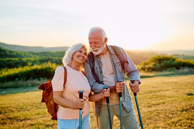 Happy senior couple embracing outdoors, hiking together with trekking poles on a hill at warm sunset. Active retirement lifestyle