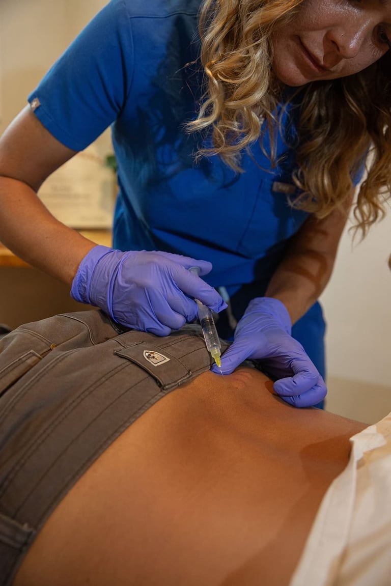 Healthcare provider in blue scrubs wearing purple gloves administering an injection to a patients arm