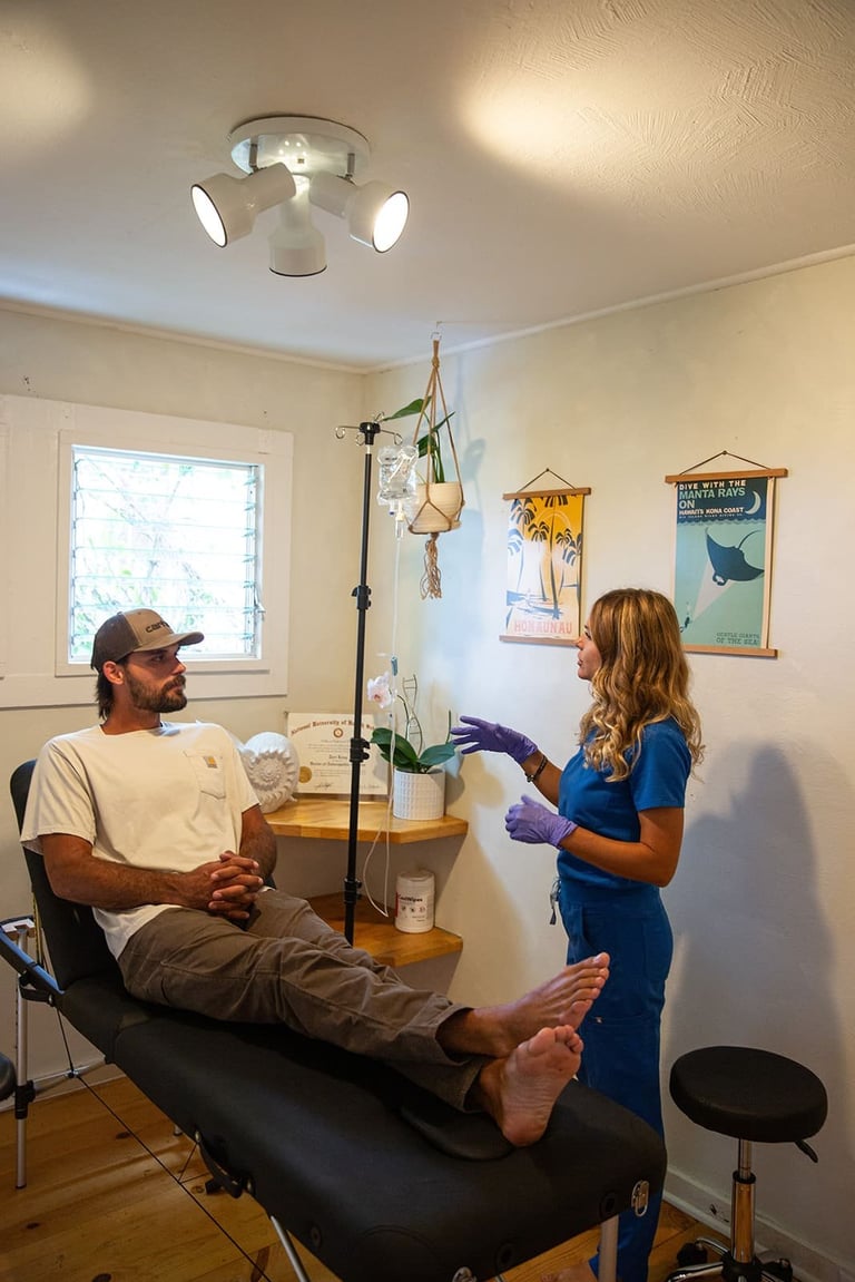 Man lying on massage table while therapist in blue shirt examines his leg in clinical room with window and wall decorations